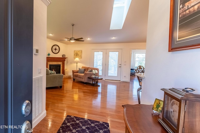 living area featuring light wood finished floors, vaulted ceiling with skylight, ceiling fan, and a glass covered fireplace