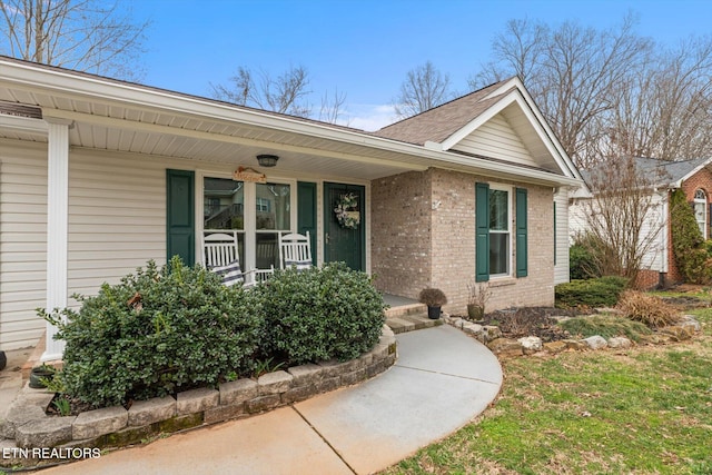 doorway to property featuring a porch and brick siding