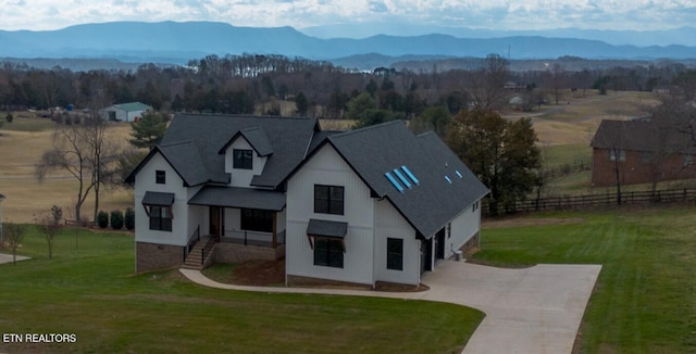 view of front of house with a shingled roof, concrete driveway, a front yard, a mountain view, and fence