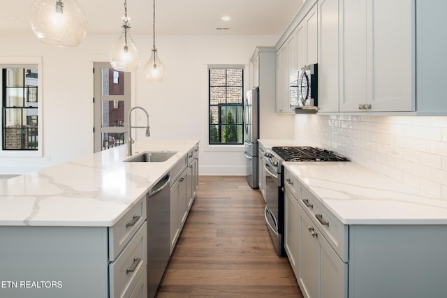 kitchen with appliances with stainless steel finishes, gray cabinets, a sink, and a center island with sink