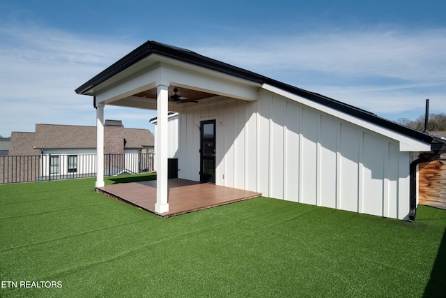 back of property featuring ceiling fan, fence, a lawn, and board and batten siding