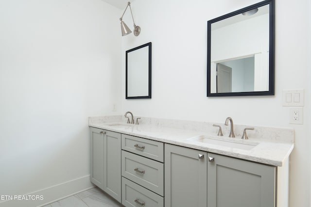 full bath featuring marble finish floor, double vanity, a sink, and baseboards