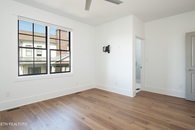 empty room featuring a ceiling fan, wood finished floors, visible vents, and baseboards