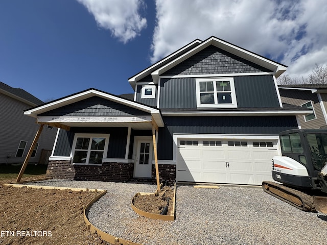 view of front facade featuring board and batten siding, gravel driveway, brick siding, and an attached garage