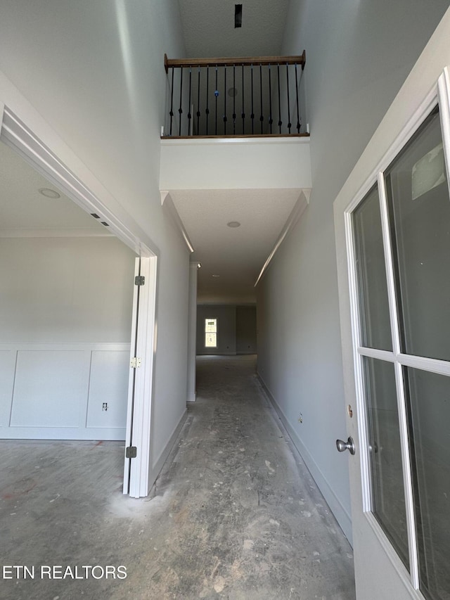 hallway with a towering ceiling, unfinished concrete floors, and baseboards