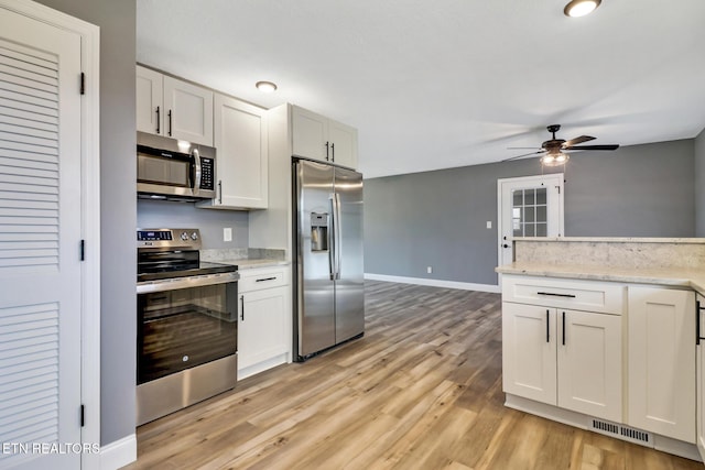 kitchen with light wood finished floors, stainless steel appliances, visible vents, a ceiling fan, and baseboards