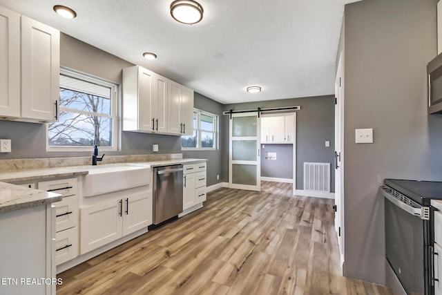 kitchen with stainless steel appliances, visible vents, a barn door, white cabinetry, and a sink