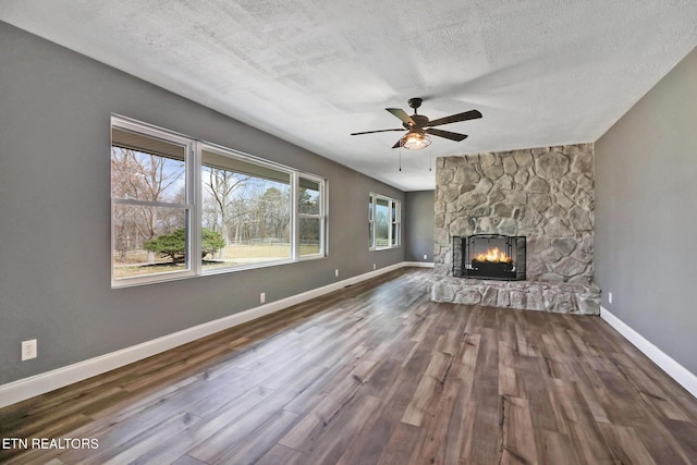 unfurnished living room featuring baseboards, a ceiling fan, wood finished floors, a textured ceiling, and a stone fireplace