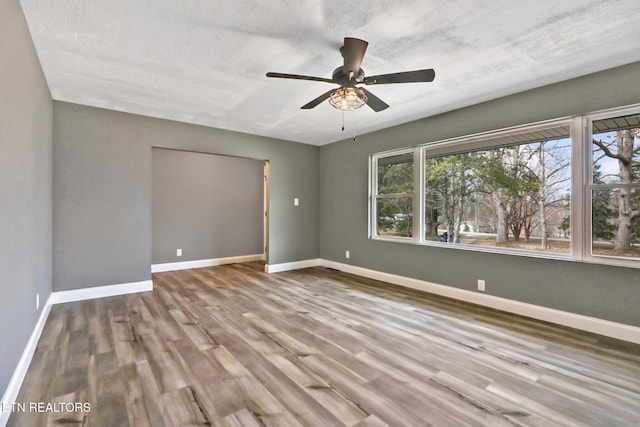 empty room with wood finished floors, a ceiling fan, and baseboards