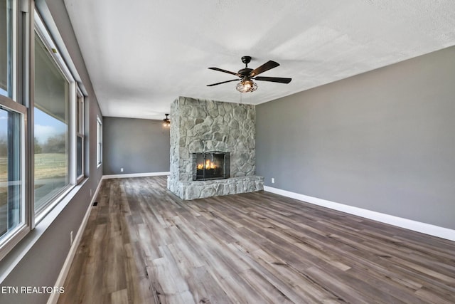 unfurnished living room featuring a fireplace, ceiling fan, a textured ceiling, wood finished floors, and baseboards