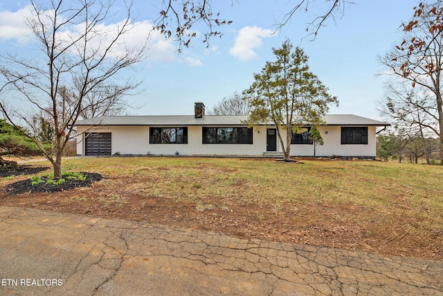 view of front facade with a chimney, an attached garage, and a front yard