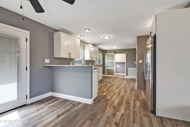 kitchen with a barn door, dark wood finished floors, a peninsula, white cabinetry, and a sink