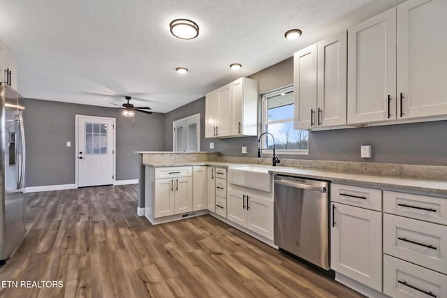 kitchen with dark wood finished floors, stainless steel appliances, white cabinets, a sink, and a peninsula