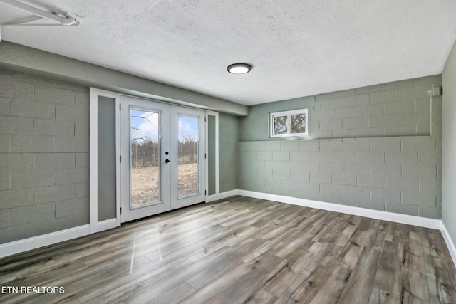 spare room featuring a textured ceiling, wood finished floors, concrete block wall, and baseboards