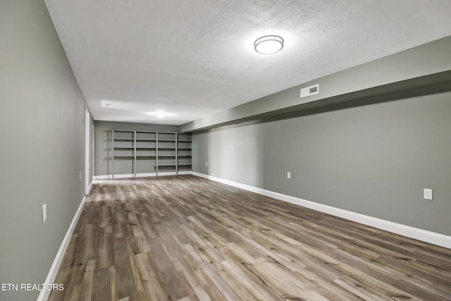 spare room featuring visible vents, a textured ceiling, baseboards, and wood finished floors