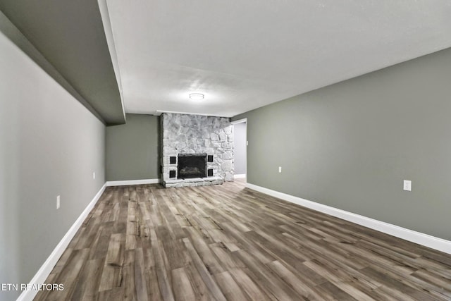 unfurnished living room with a stone fireplace, baseboards, and wood finished floors