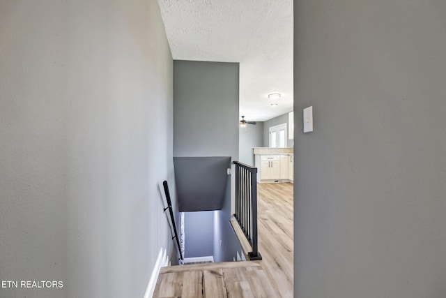 stairs with a textured ceiling, wood finished floors, and baseboards