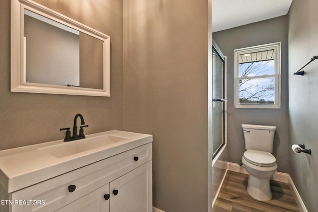 full bath featuring enclosed tub / shower combo, toilet, wood finished floors, vanity, and baseboards