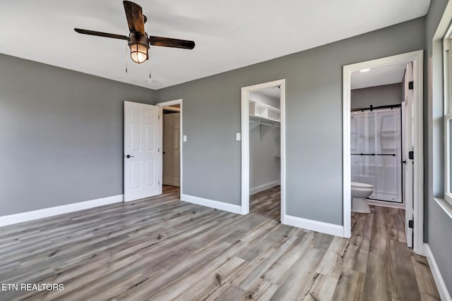 unfurnished bedroom with a walk in closet, a closet, ensuite bath, wood finished floors, and baseboards