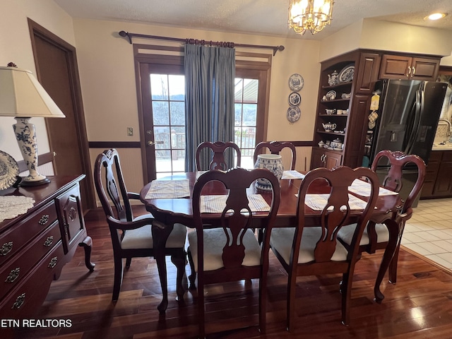 dining area featuring built in shelves, dark wood-style flooring, a wainscoted wall, a notable chandelier, and a textured ceiling