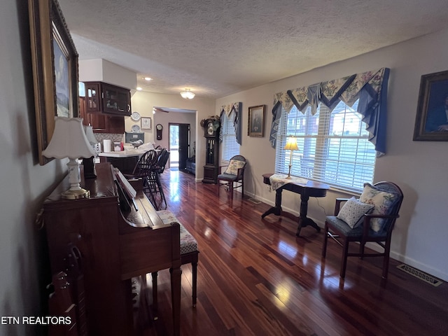 living area with a textured ceiling, dark wood finished floors, visible vents, and baseboards