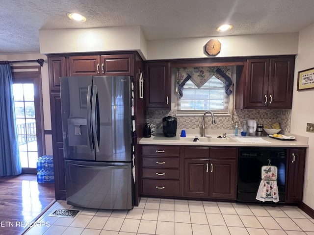 kitchen featuring black dishwasher, a sink, light countertops, refrigerator with ice dispenser, and backsplash