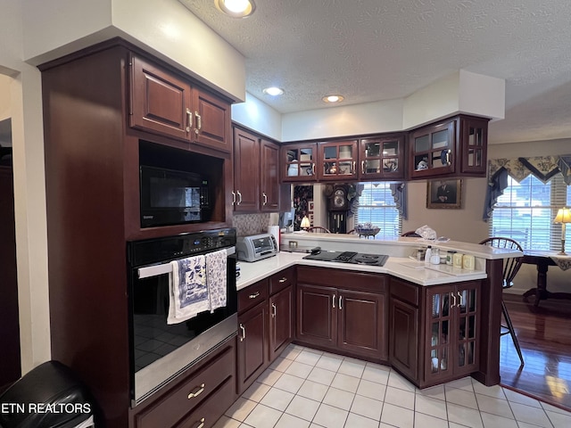 kitchen featuring a peninsula, black appliances, glass insert cabinets, and light countertops