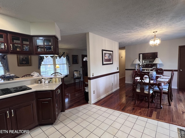 kitchen with light tile patterned floors, a chandelier, black electric cooktop, dark brown cabinetry, and light countertops