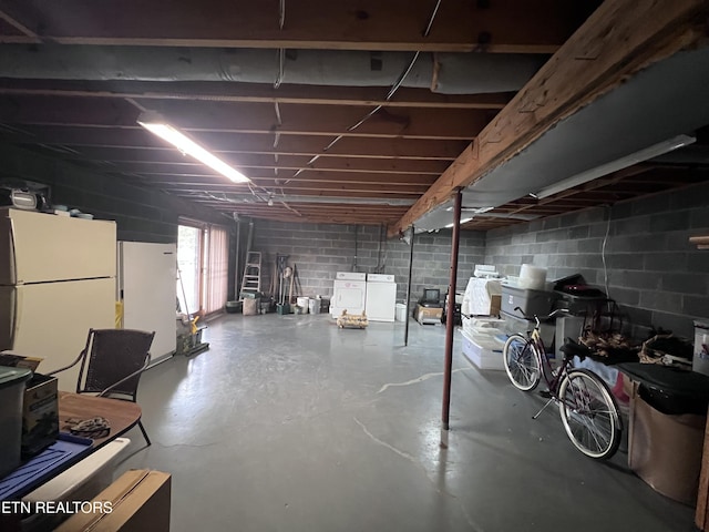 basement with freestanding refrigerator, independent washer and dryer, and concrete block wall