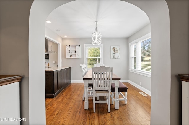 dining room with arched walkways, light wood-type flooring, visible vents, and baseboards