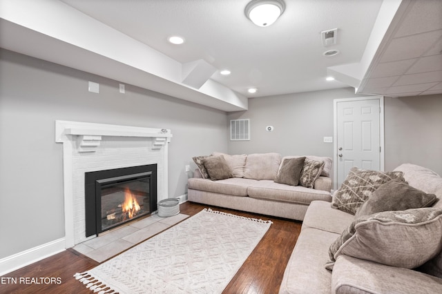 living room featuring a tile fireplace, visible vents, baseboards, and wood finished floors