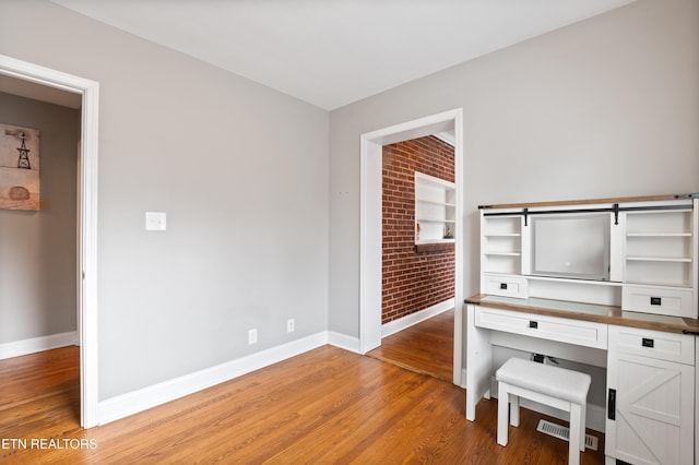 interior space with brick wall, light wood-style flooring, and baseboards