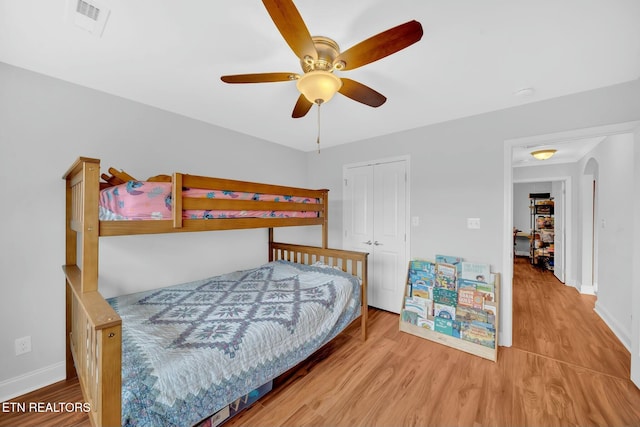 bedroom with arched walkways, a closet, wood finished floors, and baseboards