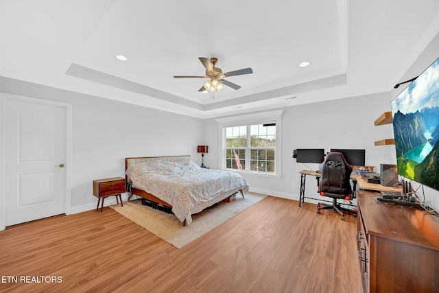 bedroom with light wood-style floors, a raised ceiling, and baseboards