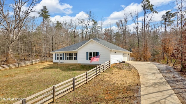 view of front of house featuring a detached garage, fence, a front lawn, and a wooded view