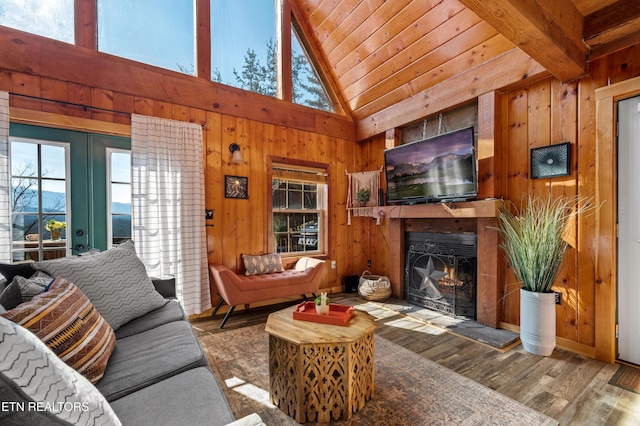 living room featuring a warm lit fireplace, wood ceiling, wooden walls, and wood finished floors