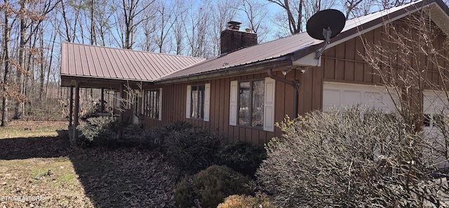 view of side of property with a garage, a chimney, metal roof, and board and batten siding