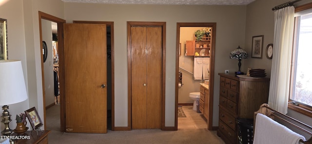 bedroom with two closets, light colored carpet, ensuite bathroom, a textured ceiling, and baseboards