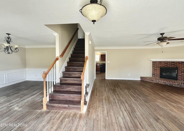 stairs featuring a brick fireplace, crown molding, ceiling fan, and wood finished floors