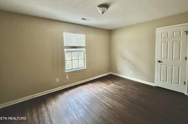 empty room featuring dark wood-style floors, visible vents, and baseboards