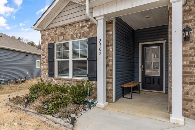 entrance to property with a porch and brick siding