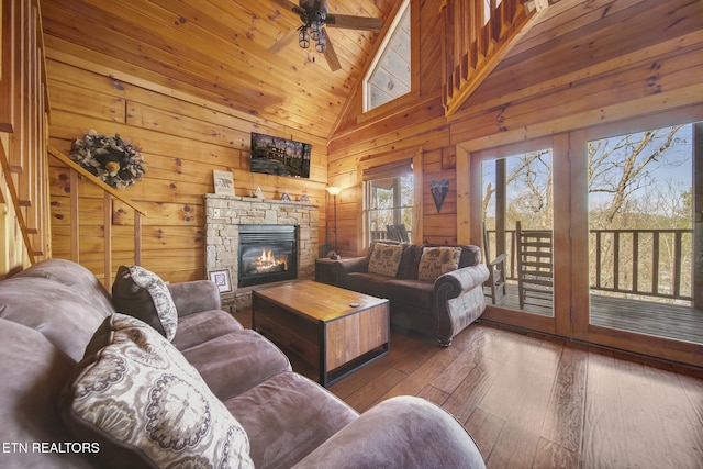 living area with hardwood / wood-style floors, high vaulted ceiling, a fireplace, ceiling fan, and wood walls