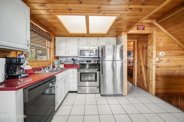 kitchen featuring a sink, white cabinetry, stainless steel appliances, wooden walls, and wood ceiling