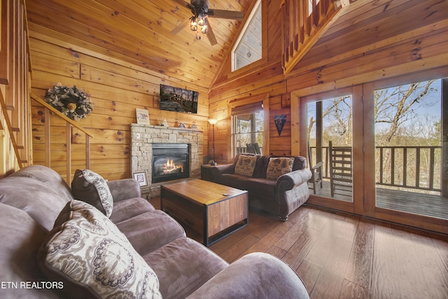 living room with a ceiling fan, wood walls, a stone fireplace, hardwood / wood-style flooring, and lofted ceiling