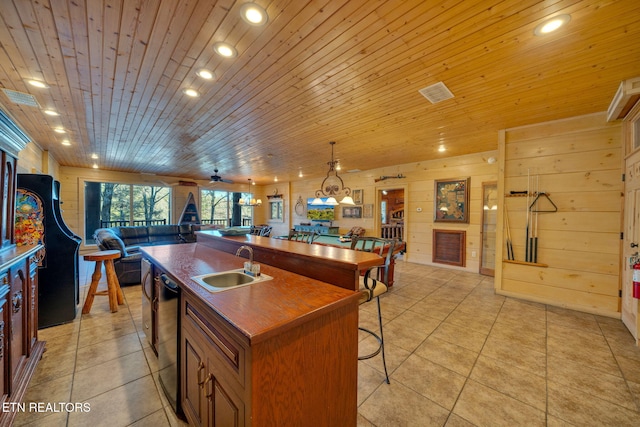 kitchen with wooden ceiling, open floor plan, a kitchen island with sink, wood walls, and a sink