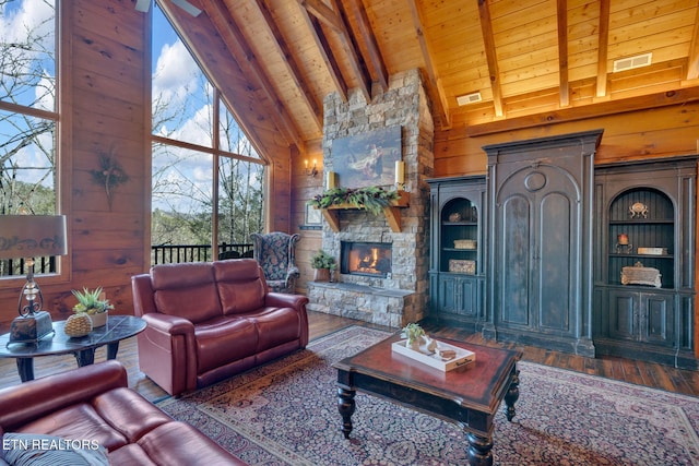 living area with a stone fireplace, wooden ceiling, wood walls, wood finished floors, and beam ceiling