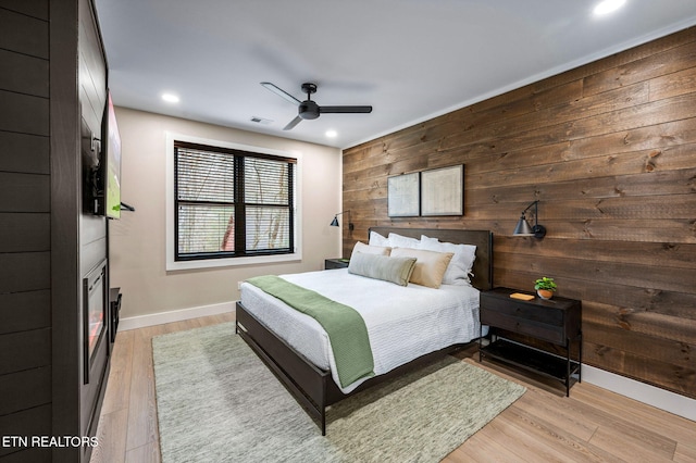 bedroom featuring visible vents, light wood-style floors, wood walls, and a fireplace