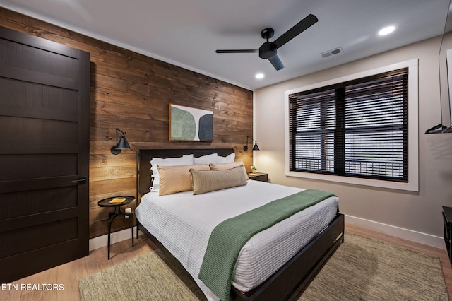 bedroom with wooden walls, wood finished floors, visible vents, baseboards, and recessed lighting