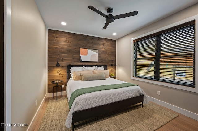 bedroom featuring wood finished floors, recessed lighting, wooden walls, baseboards, and an accent wall