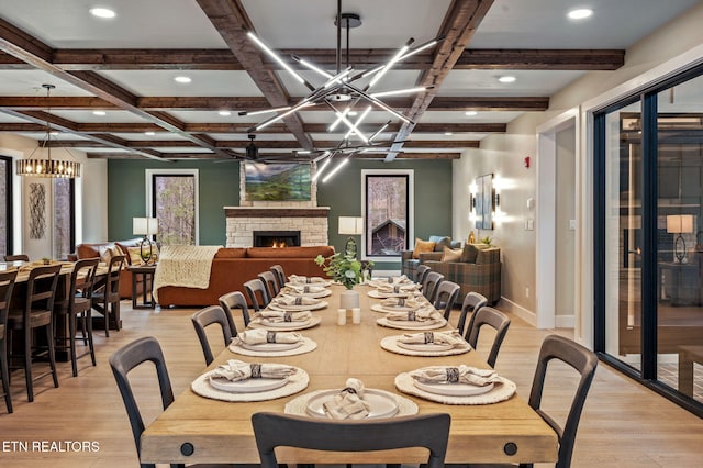 dining area with beamed ceiling, light wood-style flooring, a fireplace, and coffered ceiling